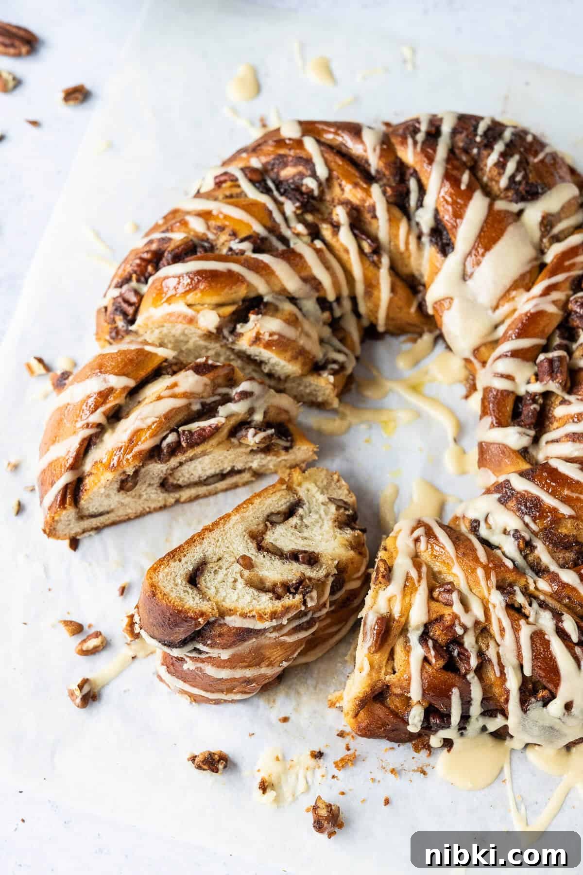 Close up of sliced maple pecan bread wreath drizzled with maple glaze on a sheet of baking parchment.