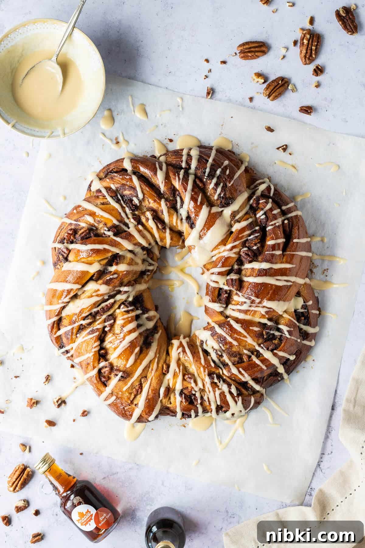 Maple pecan bread wreath from above on a sheet of baking parchment on a grey background.