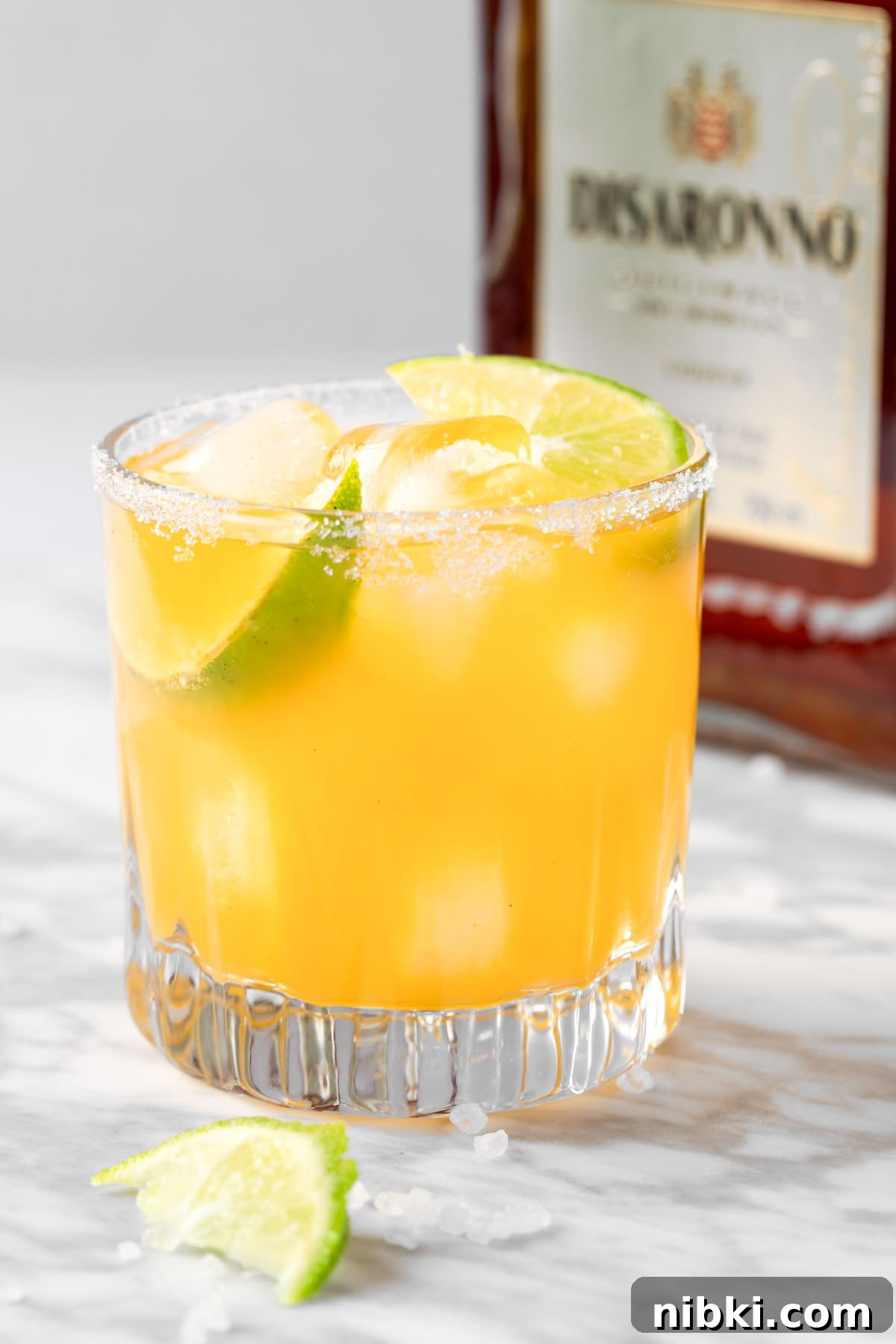 An Olive Garden Italian Margarita garnished with lime, with an amaretto bottle in the background.