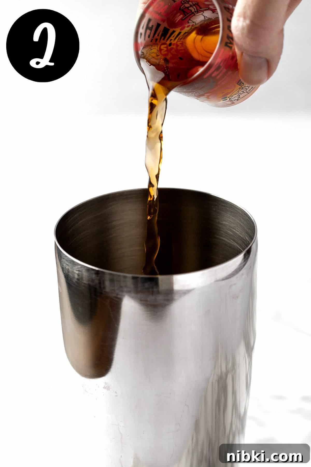 Pouring the Amaretto into a metal cocktail shaker.