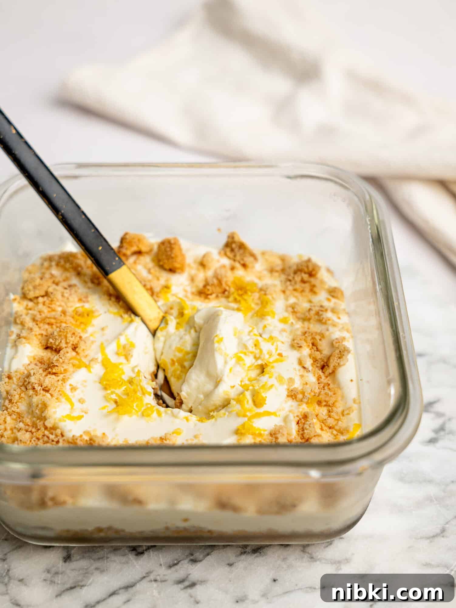 Side view of lemon cheesecake overnight Weet-Bix showing layers of Weet-Bix base and creamy lemon cheesecake filling, topped with biscuit crumbs and lemon zest.
