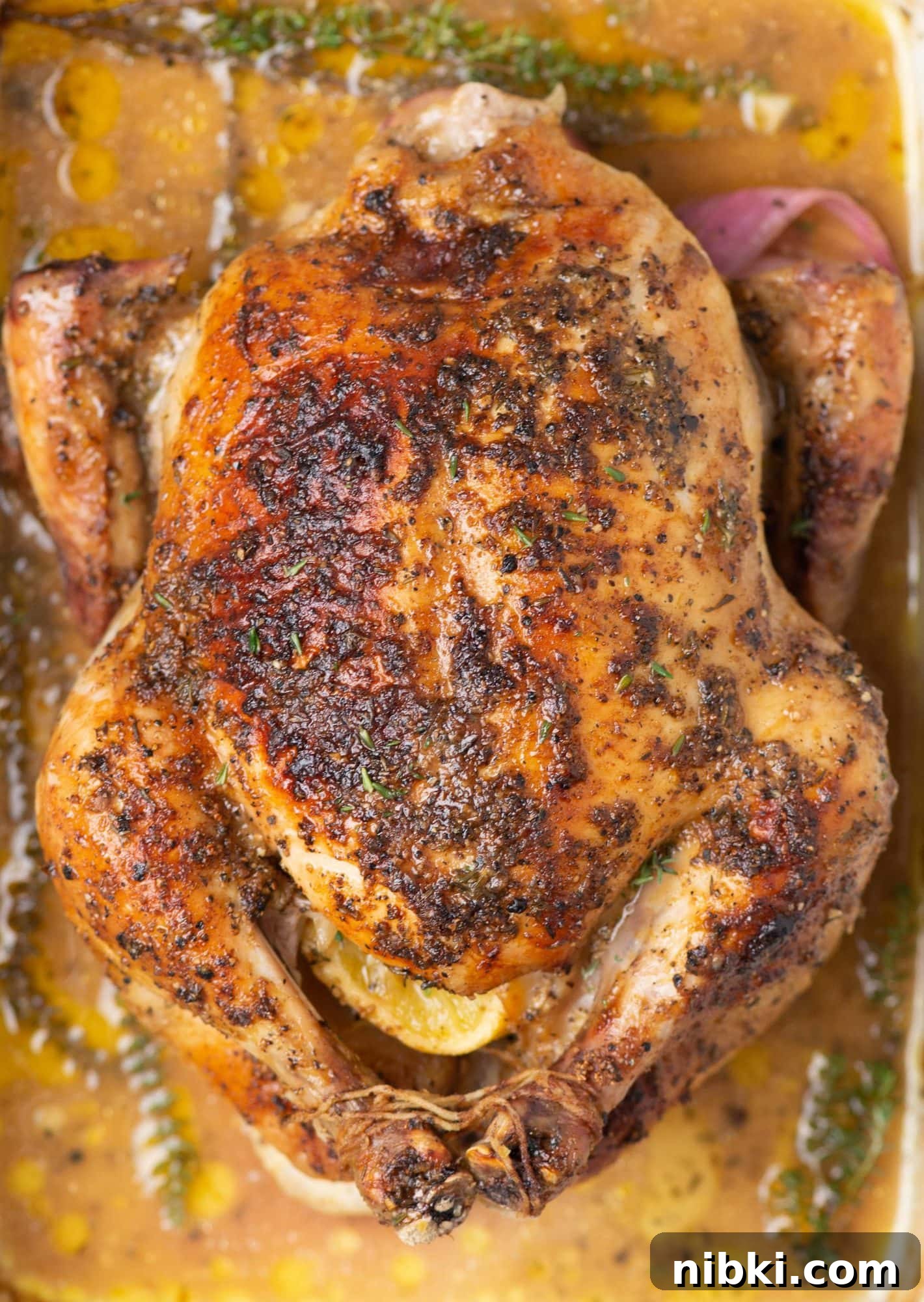 Cover photo of roast chicken on pan Picture of chicken roasted on a pan with lemon wedges inside and thyme and gravy in the pan.