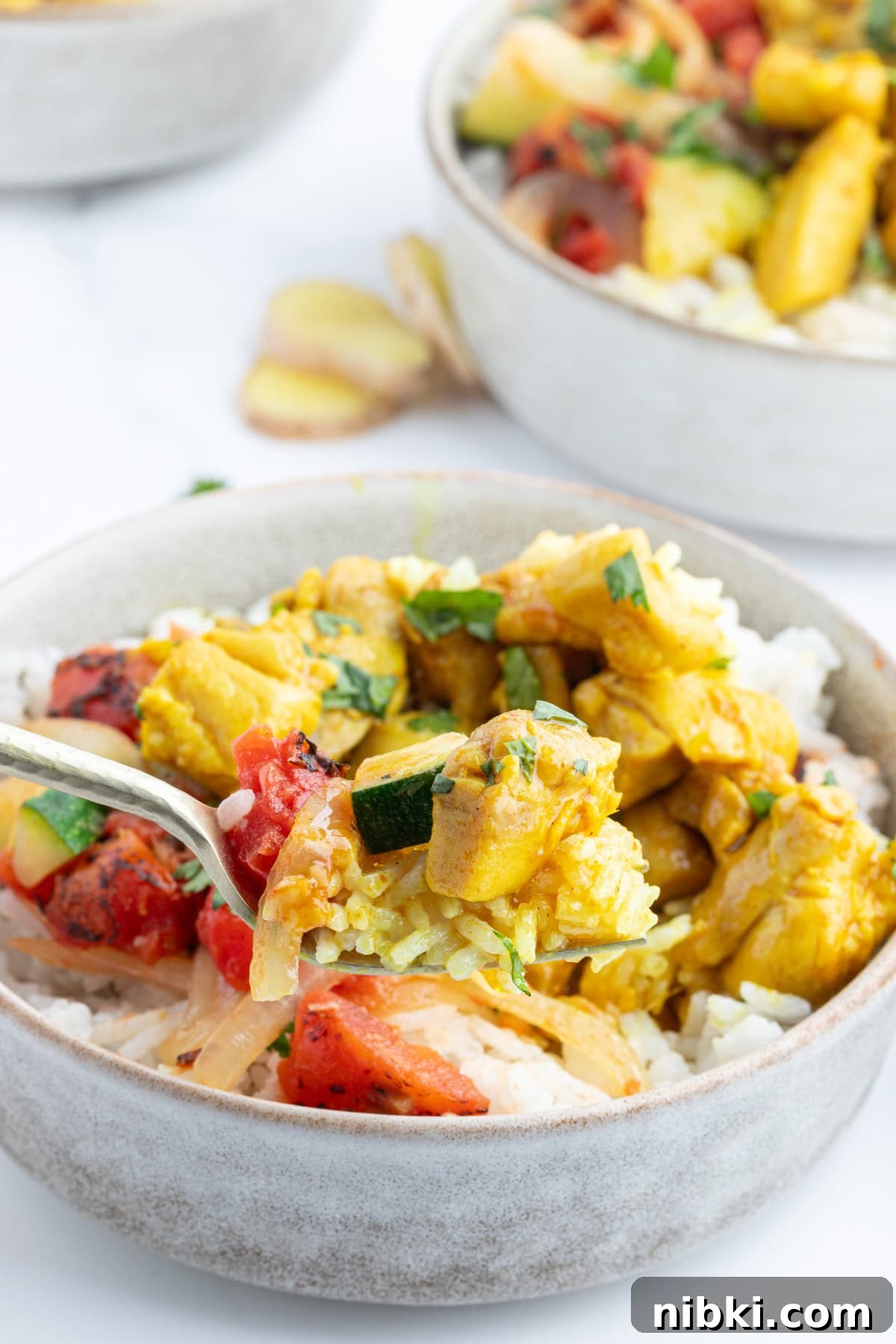 Chicken curry bowls with coconut rice, spiced chicken and a flavorful tomato mixture. Cozy, balanced and perfect for dinner! fork in chicken curry bowl