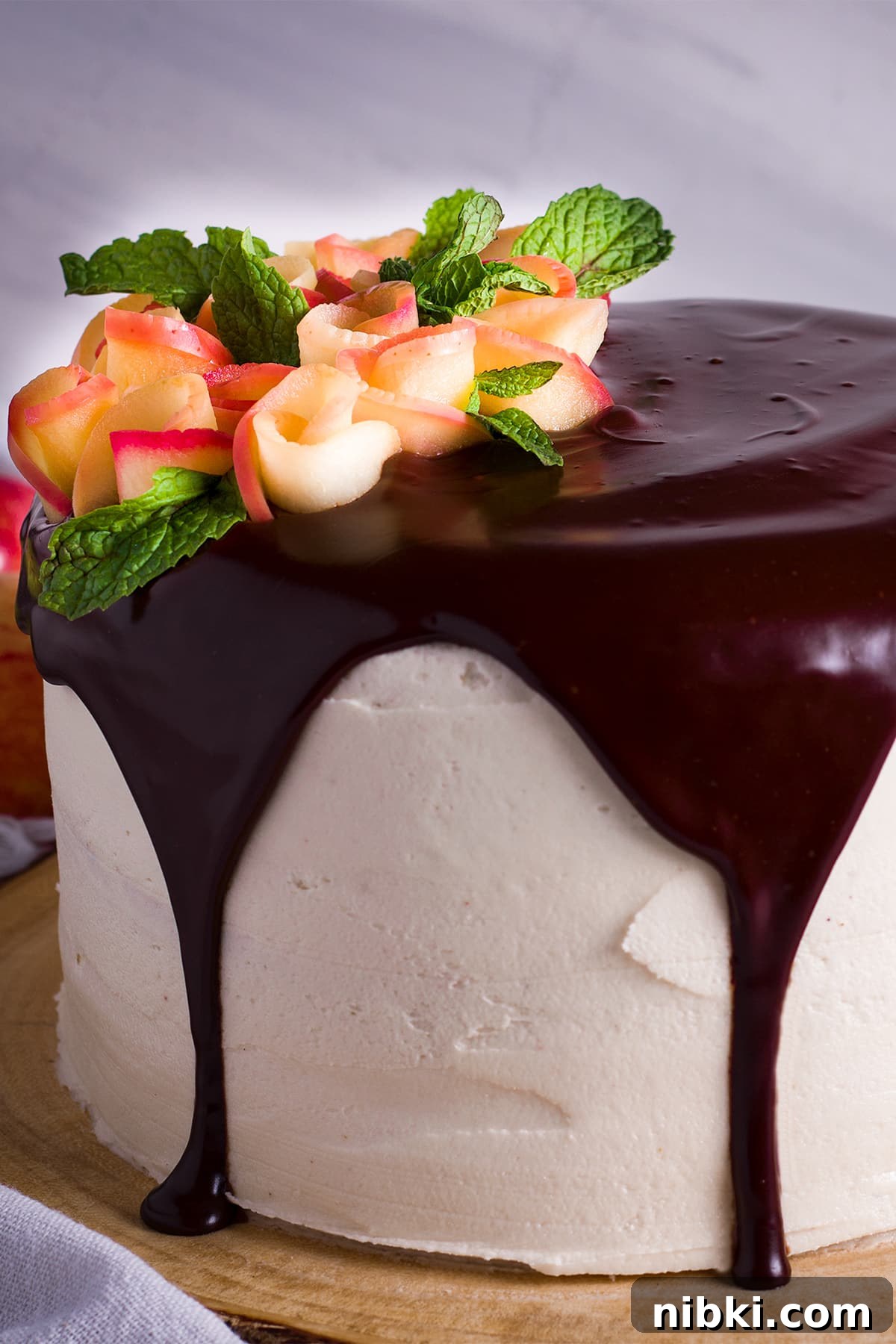 Spiced Apple Cider Cake with Cider Buttercream 2 An apple Cake frosted with Cider Buttercream, covered with chocolate ganache, and decorated with apple roses on a wood cake stand.