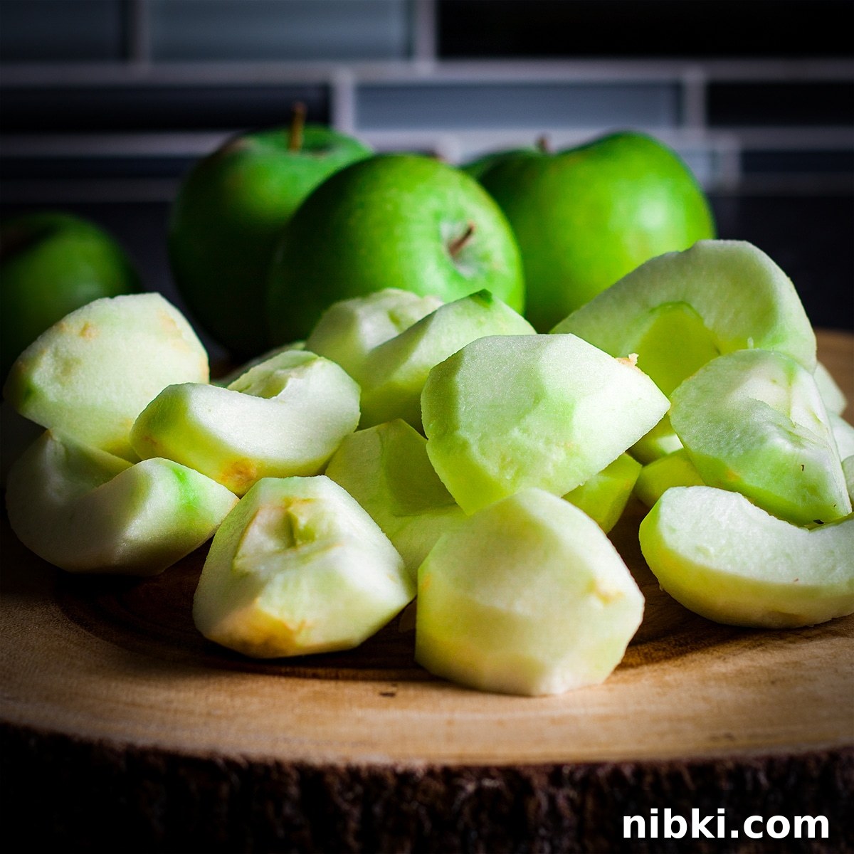 Spiced Apple Cider Cake with Cider Buttercream 7 A pile of partially peeled and sliced green apples on a wood cutting board.