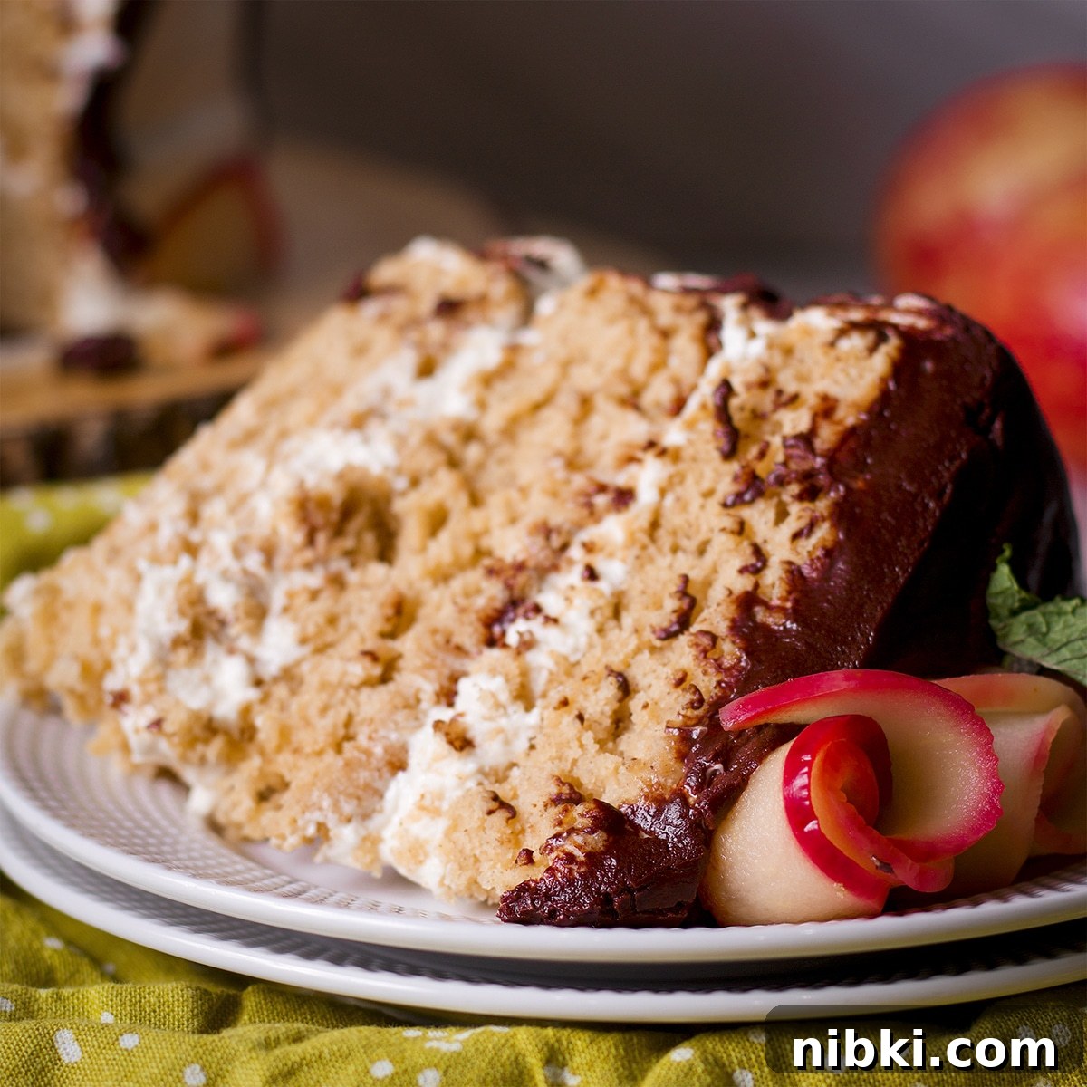Spiced Apple Cider Cake with Cider Buttercream 8 A slice of 3- layer apple cake filled and frosted with cider buttercream. The slice is laying on its side on a white plate.