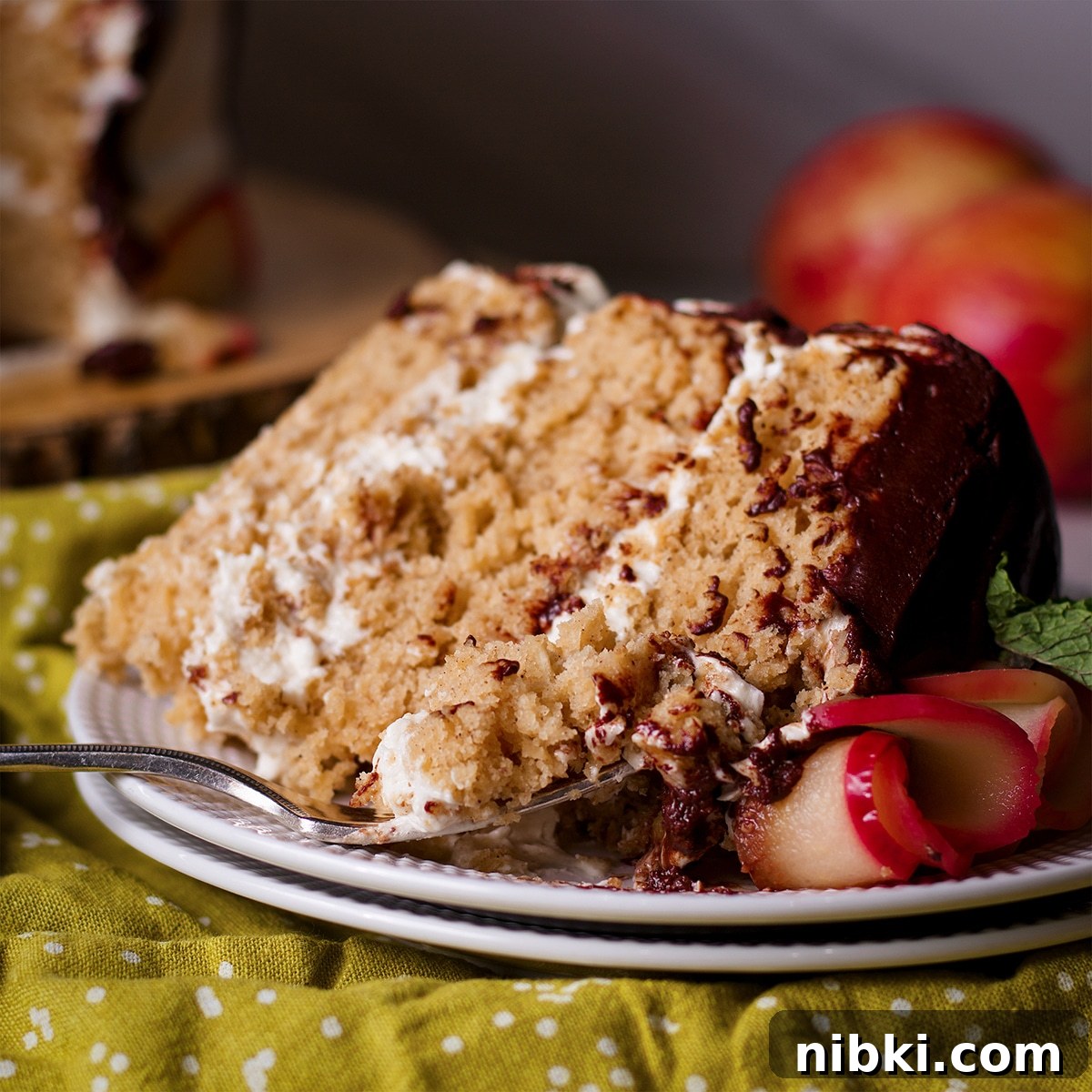 Spiced Apple Cider Cake with Cider Buttercream 17 A slice of 3-layer apple cider cake on a white plate. Someone is using a fork to cut a bite of cake from the slice.