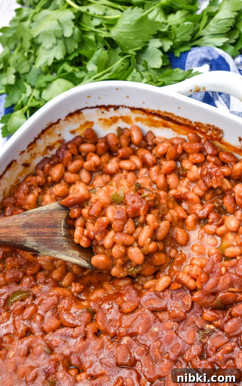 a wooden spoon scooping the best canned baked beans out of a white casserole dish