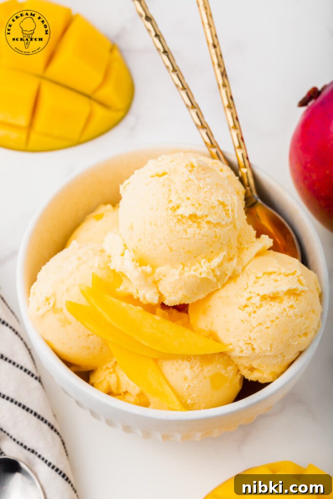 Homemade Mango Ice Cream Recipe 5 a large bowl of scooped mango ice cream topped with thinly sliced fresh mangoes. There are two gold spoons in the bowl.