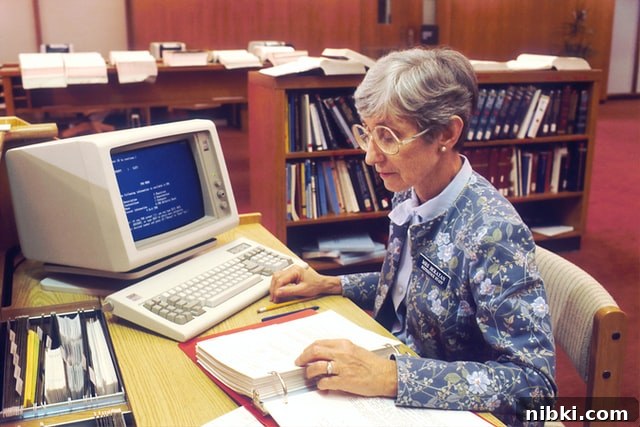 Librarian sitting at desk with old style computer on desk.