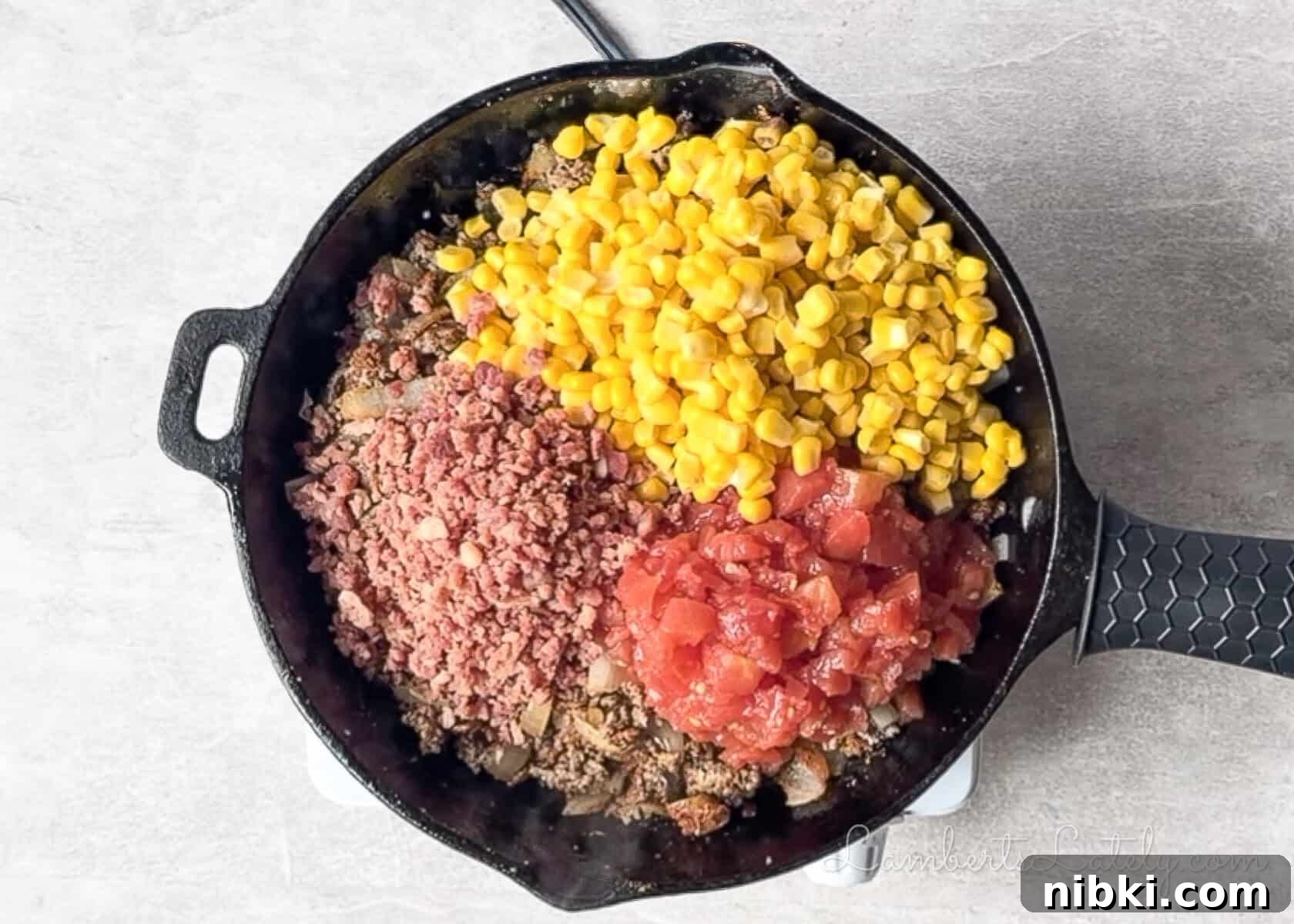 corn, tomatoes, and bacon added to a cast iron skillet.