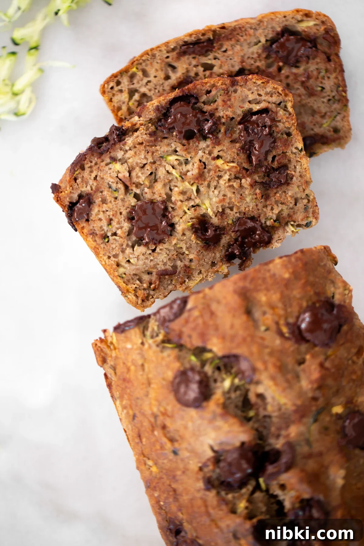 Overhead shot of 2 slices of healthy zucchini banana bread with the rest of the loaf on a white marble background