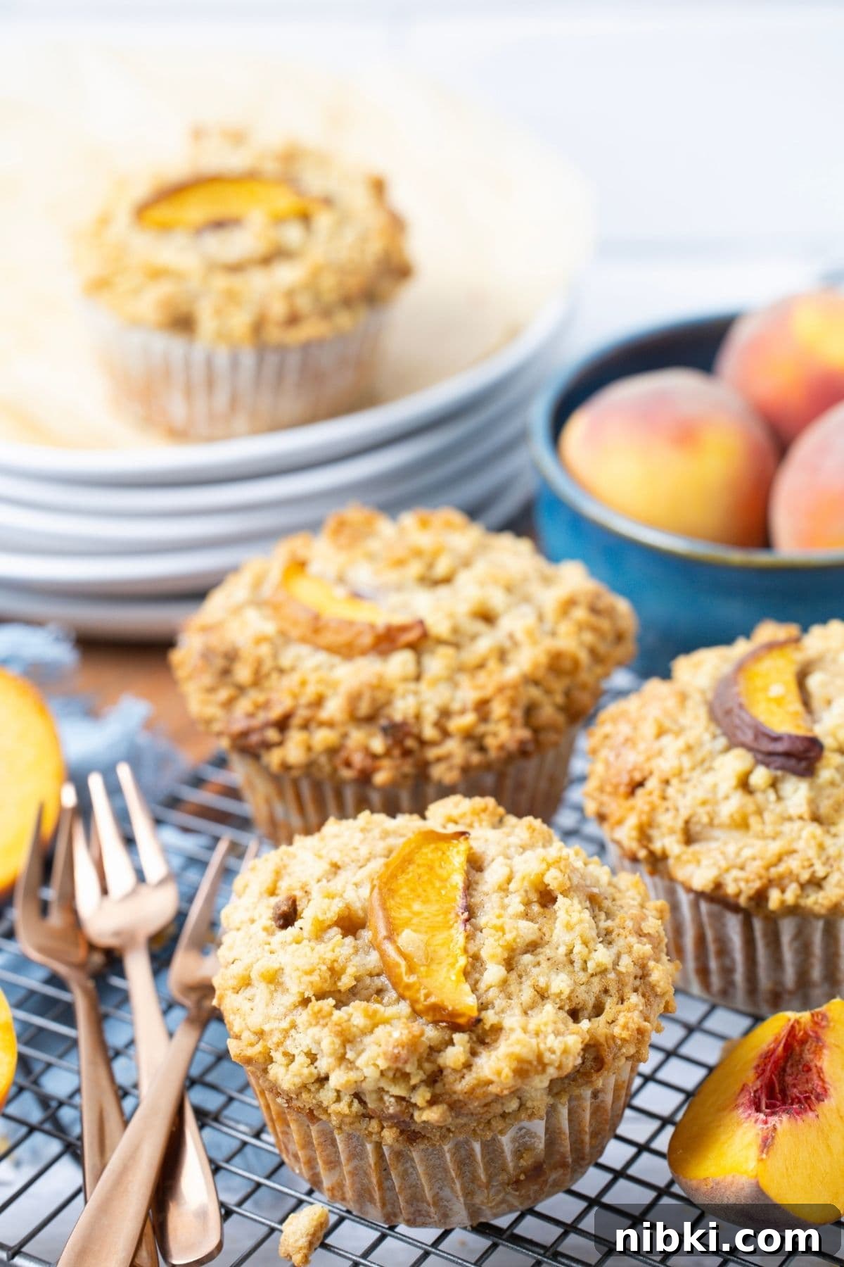 Sourdough Peach Cobbler Muffins Recipe 3 Sourdough peach cobbler muffins on a wire rack next to plates and forks for serving.