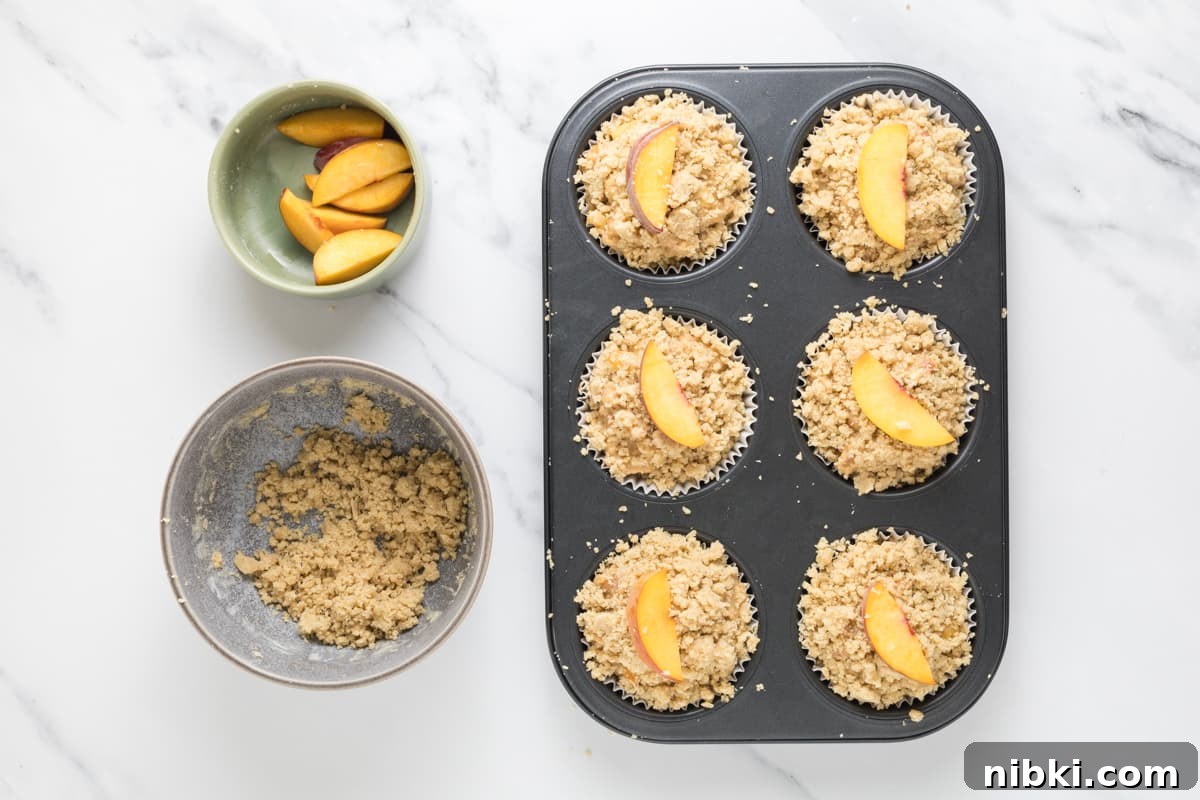 Sourdough Peach Cobbler Muffins Recipe 8 Sourdough peach cobbler muffin batter in a muffin tin with homemade streusel and a peach slice on top, ready to be baked.