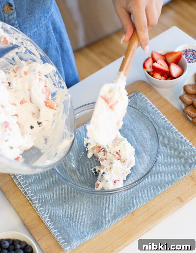 Patriotic Red, White and Blue Cheesecake Dip for 4th of July 7 Transferring a creamy fruit mixture with berries from a bowl into a glass dish.