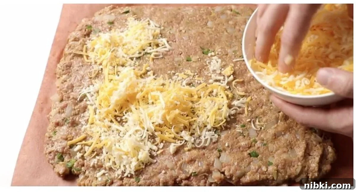 Smoked Meatloaf Recipe with Brown Sugar Glaze 9 Person sprinkling shredded cheese into a meatloaf.