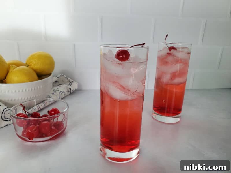 Two dirty Shirley drinks next to a bowl of maraschino cherries and a bowl of lemons