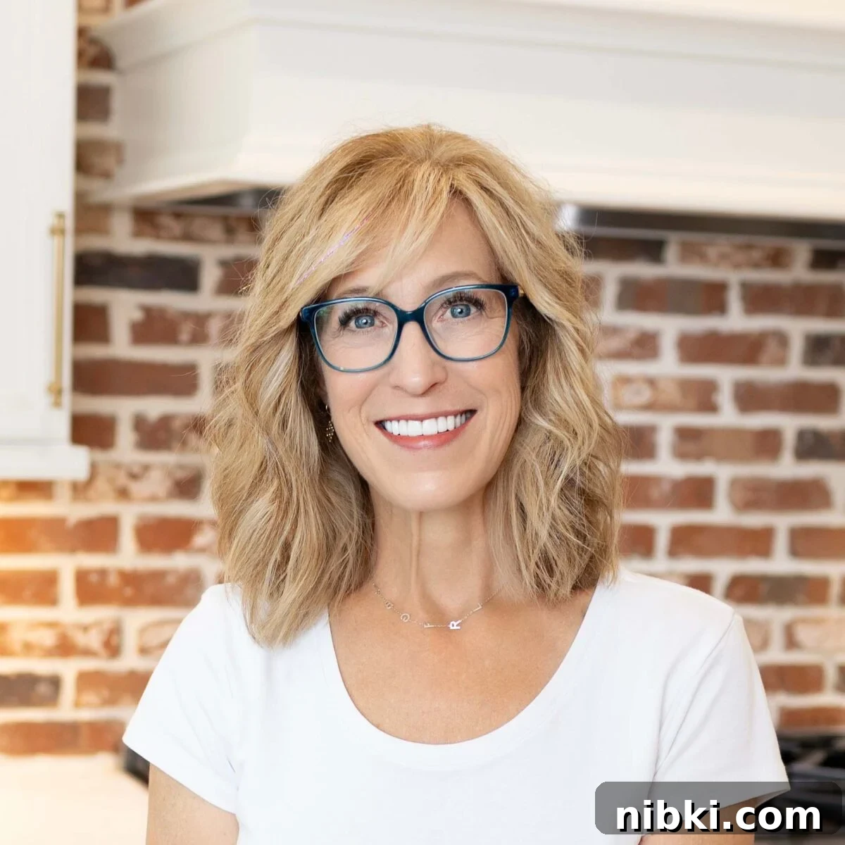 No-Bake Key Lime Icebox Cake Recipe 4 Person with shoulder-length blond hair and blue glasses smiling indoors in front of a red brick wall.
