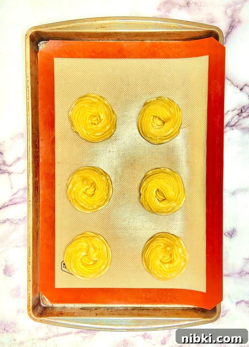 Zeppole di San Giuseppe: Classic St. Joseph's Pastry Recipe 7 Dough piped onto a baking sheet lined with a silicone mat.