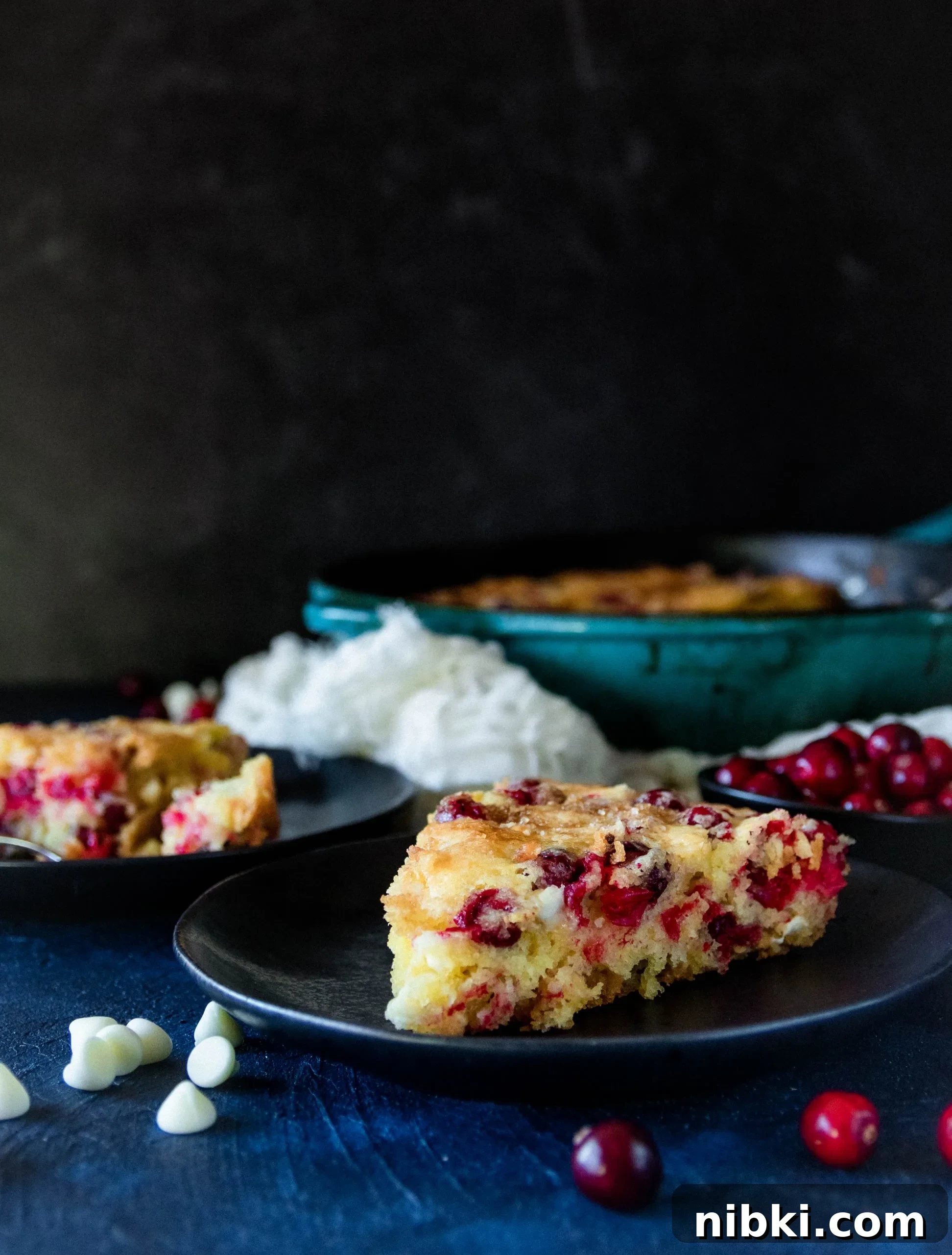 Fresh Cranberry Skillet Cake Recipe 5 slice of cranberry skillet cake on a black plate with the rest of the cake in the background