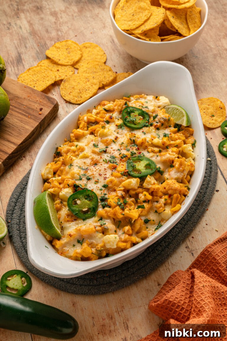 Creamy Mexican Street Corn Dip Recipe 2 An overhead view of cheesy Mexican corn dip served in a white baking dish, surrounded by tortilla chips and fresh lime wedges.