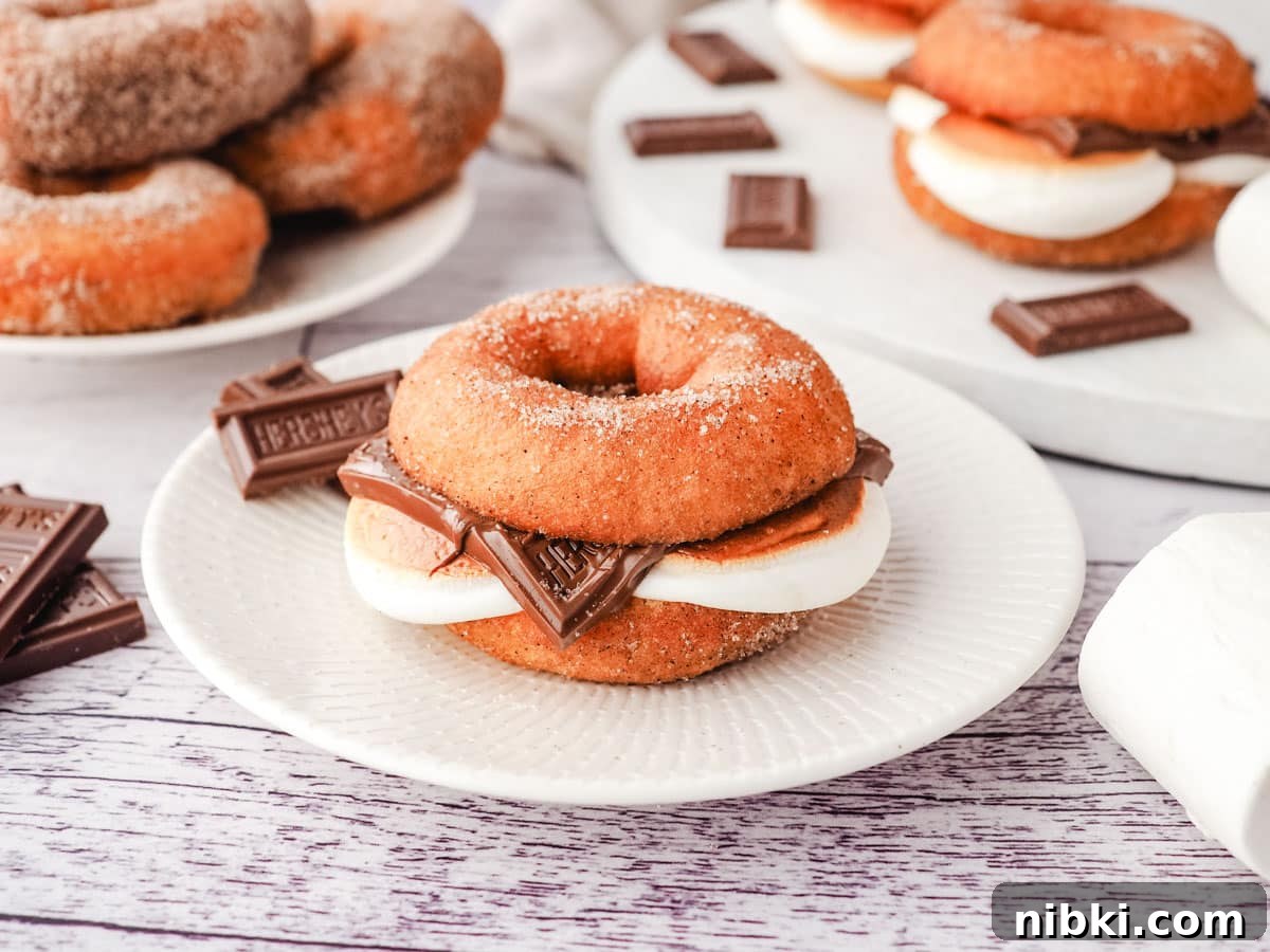 S'mores Donuts Recipe: Chocolate, Graham and Toasted Marshmallow 7 A smore donut on a plate with pieces of Hershey’s chocolate on the side and more smore donuts on a serving board in the background.