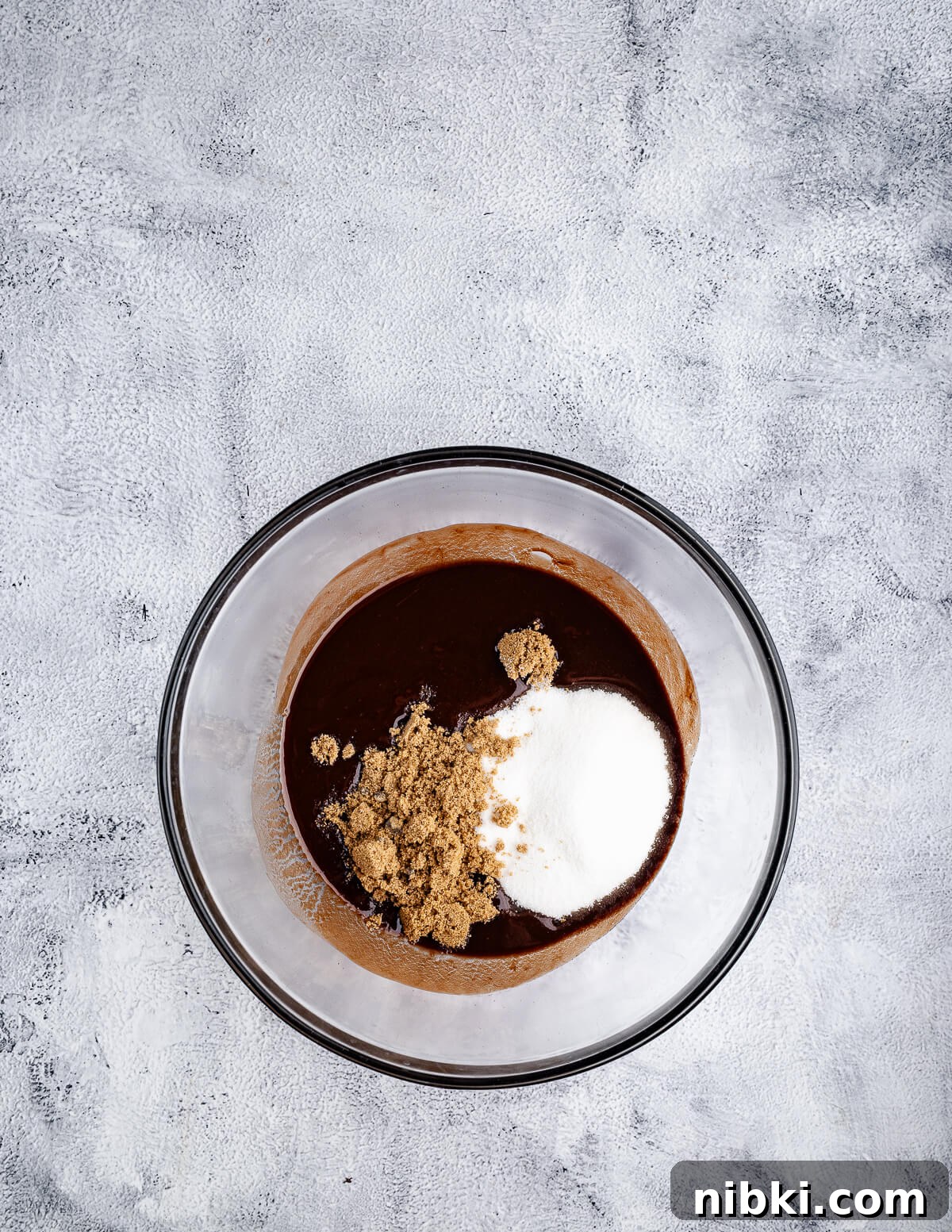 a bowl of melted chocolate and butter with sugar and brown sugar on top.