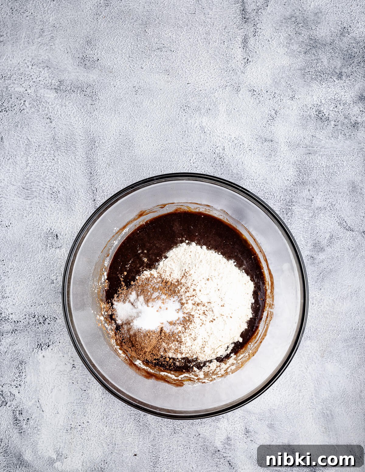 a bowl of melted chocolate, eggs, and sugar mixed together with flour and cocoa powder on top.