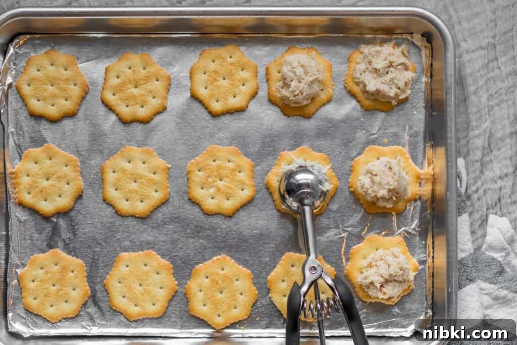 Mini Tuna Melt Bites on Crispy Crackers 4 crackers on a sheet pan with tuna being scooped on top with cookie scoop