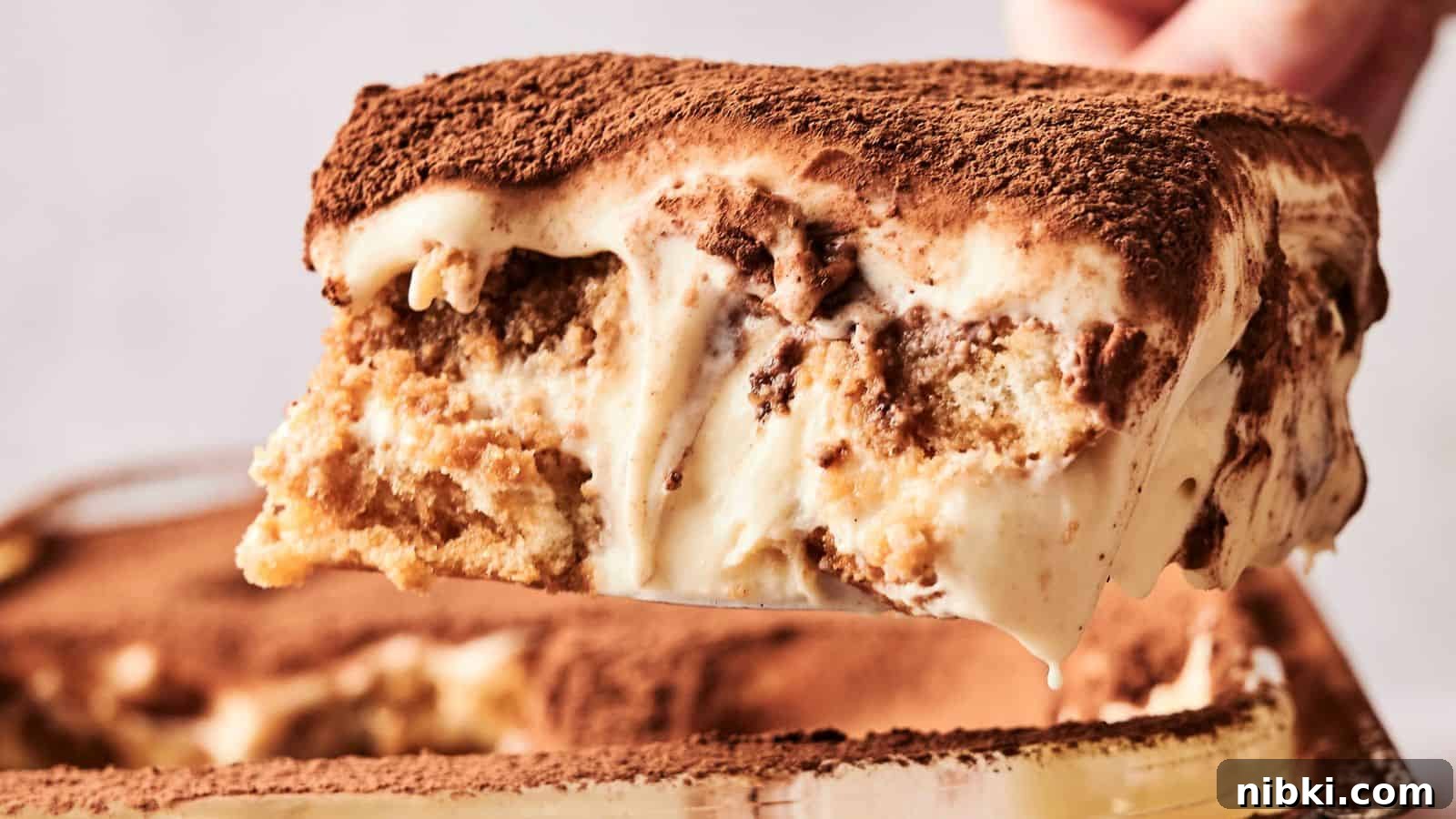 33 Christmas Potluck Recipes to Bring December Magic 16 A slice of tiramisu is being lifted from the dish, showcasing layers of coffee-soaked ladyfingers and creamy mascarpone, topped with cocoa powder.