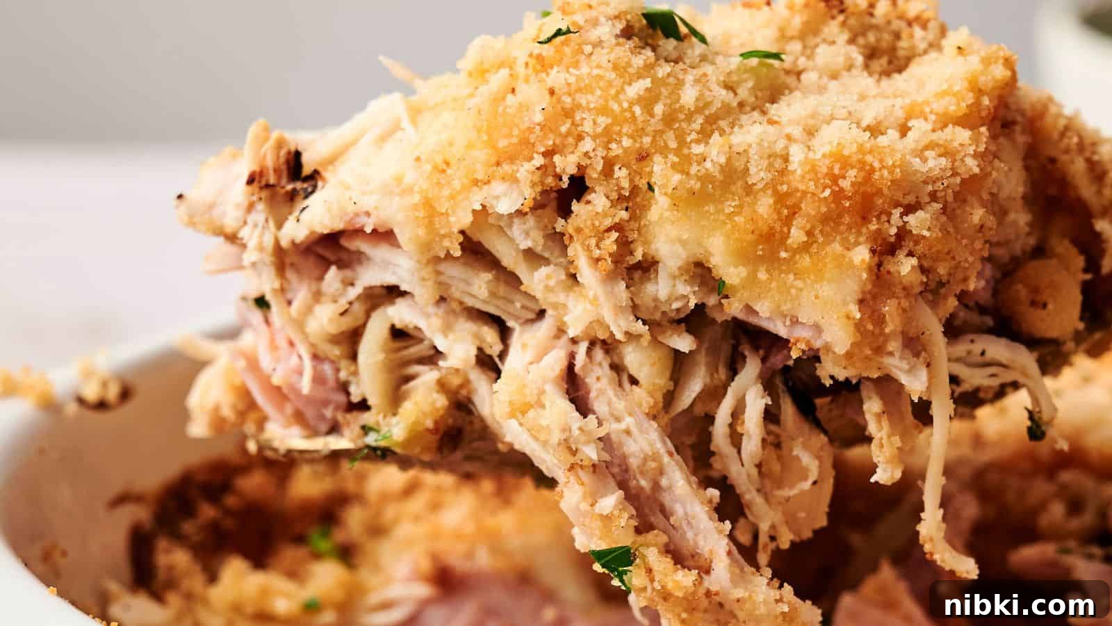 33 Christmas Potluck Recipes to Bring December Magic 18 Close-up of a serving of chicken cordon bleu casserole with shredded chicken, ham, melted cheese, and breadcrumb topping, garnished with parsley.