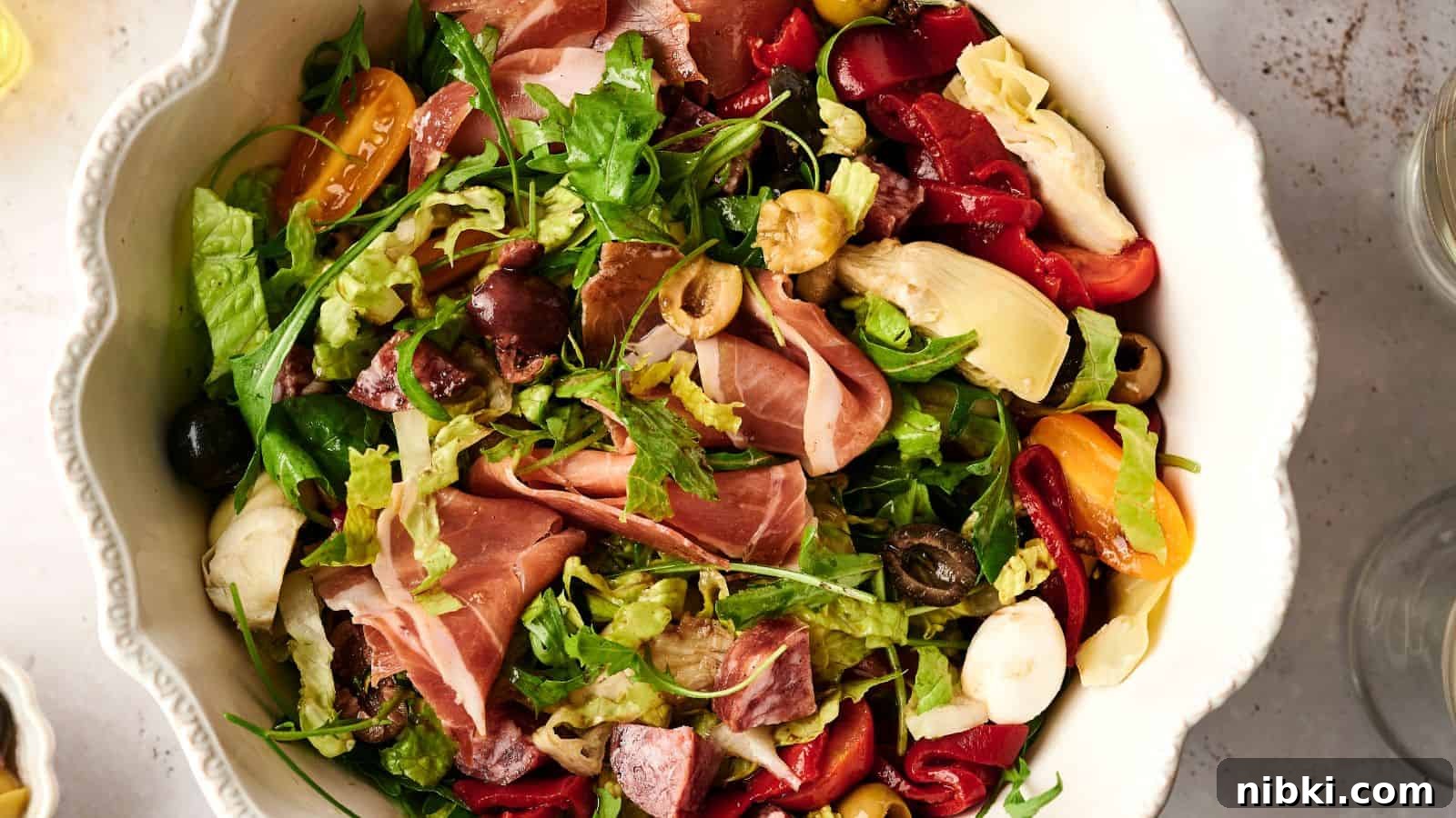 33 Christmas Potluck Recipes to Bring December Magic 22 A bowl of salad with mixed greens, prosciutto, cherry tomatoes, olives, artichokes, and roasted red peppers.
