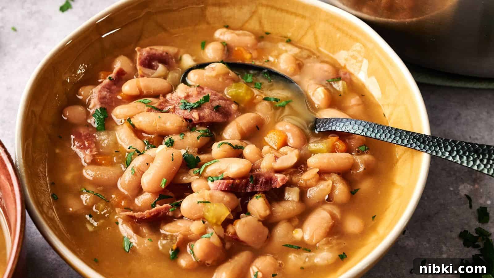 33 Christmas Potluck Recipes to Bring December Magic 23 A bowl of white bean soup with pieces of ham, garnished with chopped parsley, and a spoon resting in the bowl.