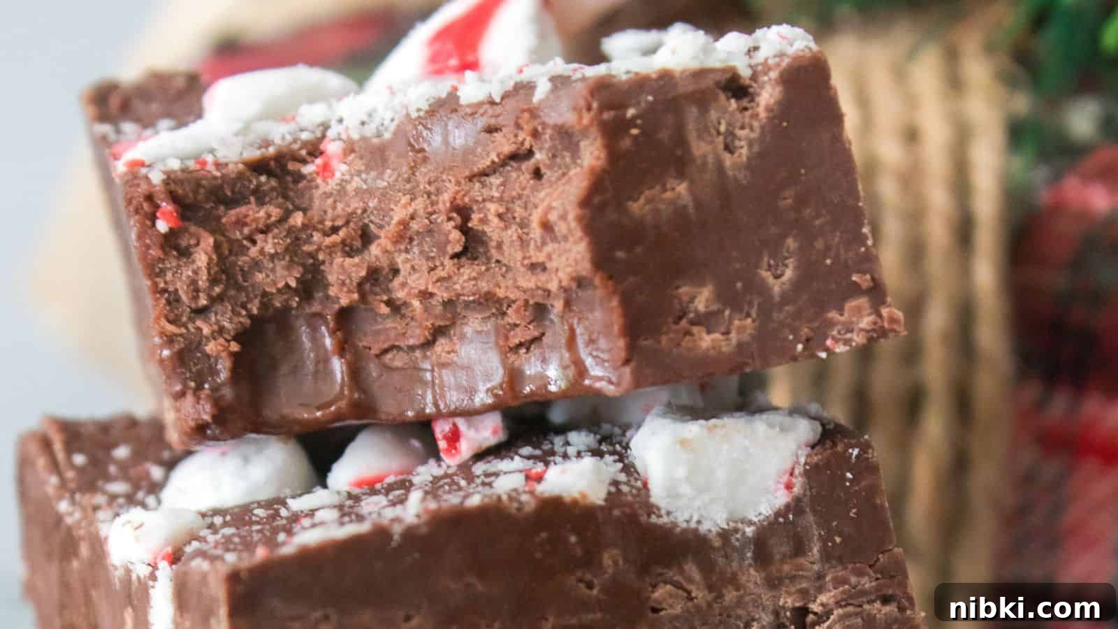 33 Christmas Potluck Recipes to Bring December Magic 3 Close-up of two stacked pieces of chocolate peppermint fudge, with visible crushed peppermint candy on top.