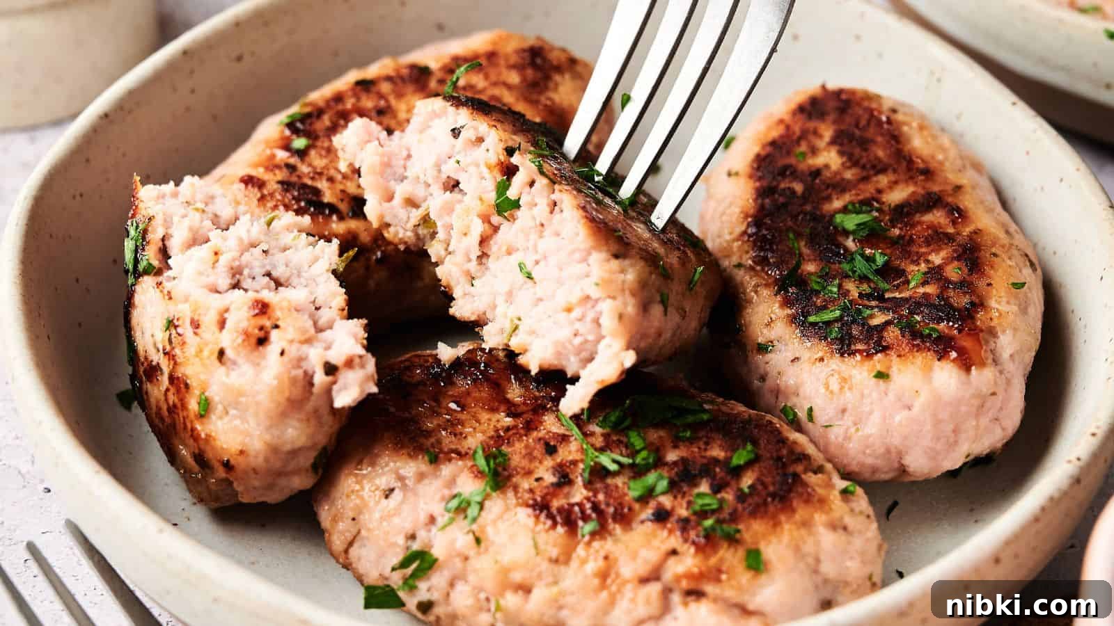 33 Christmas Potluck Recipes to Bring December Magic 30 Four browned sausage patties garnished with chopped herbs on a plate, with a fork breaking one open to show the inside.