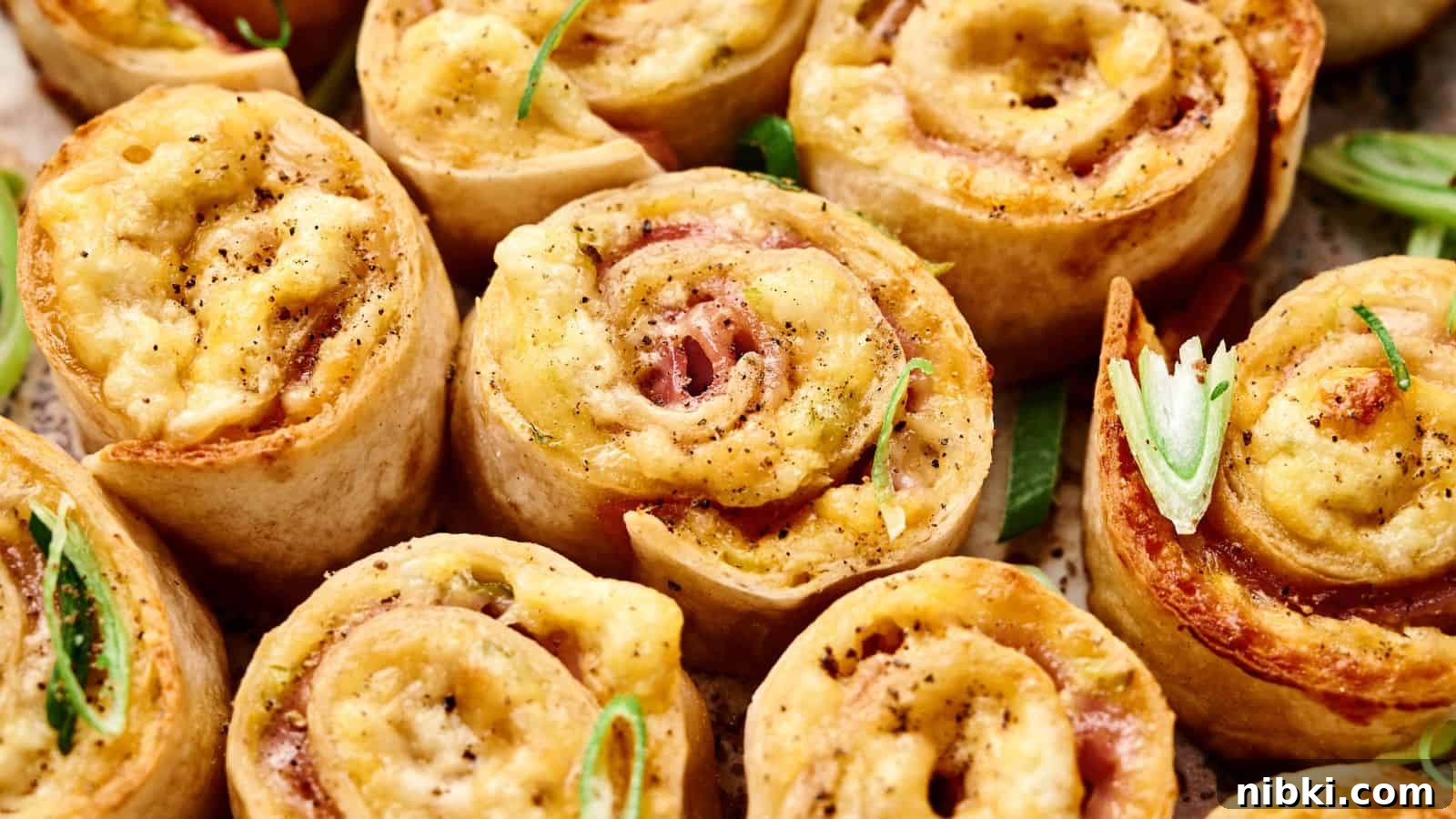 33 Christmas Potluck Recipes to Bring December Magic 31 Close-up of baked pinwheel appetizers filled with cheese and ham, topped with black pepper and garnished with sliced green onions.