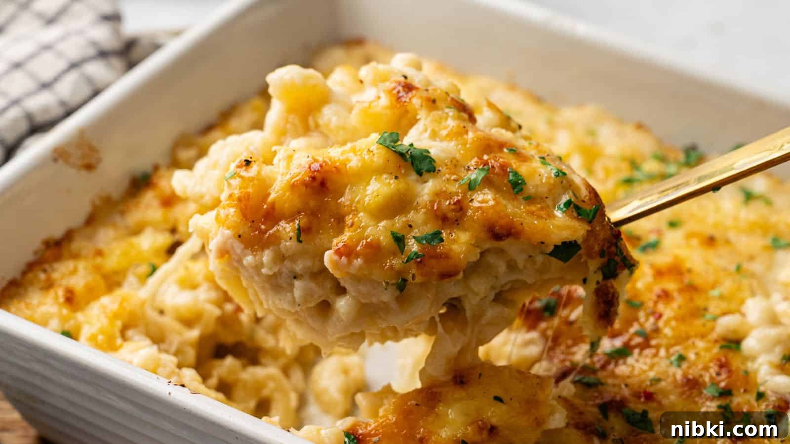33 Christmas Potluck Recipes to Bring December Magic 4 A close-up of a serving of baked macaroni and cheese being lifted from a casserole dish, topped with melted cheese and garnished with chopped herbs.