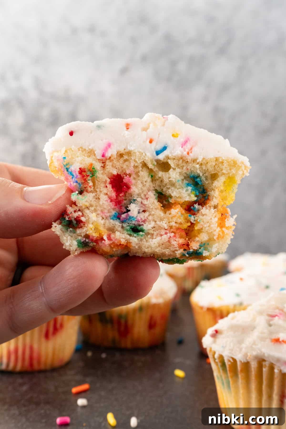 holding a birthday funfettie cupcake cut in half.