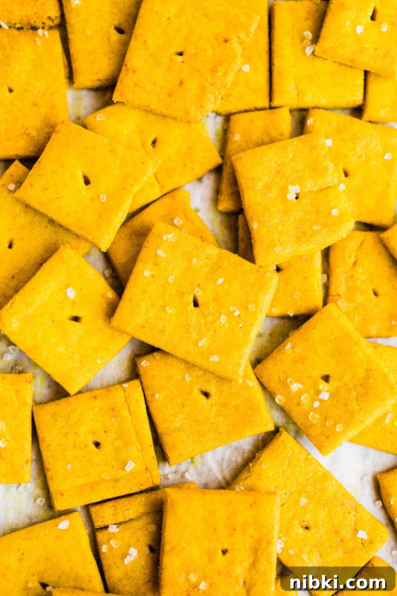Cheese crackers with sea salt spread out on parchment paper.