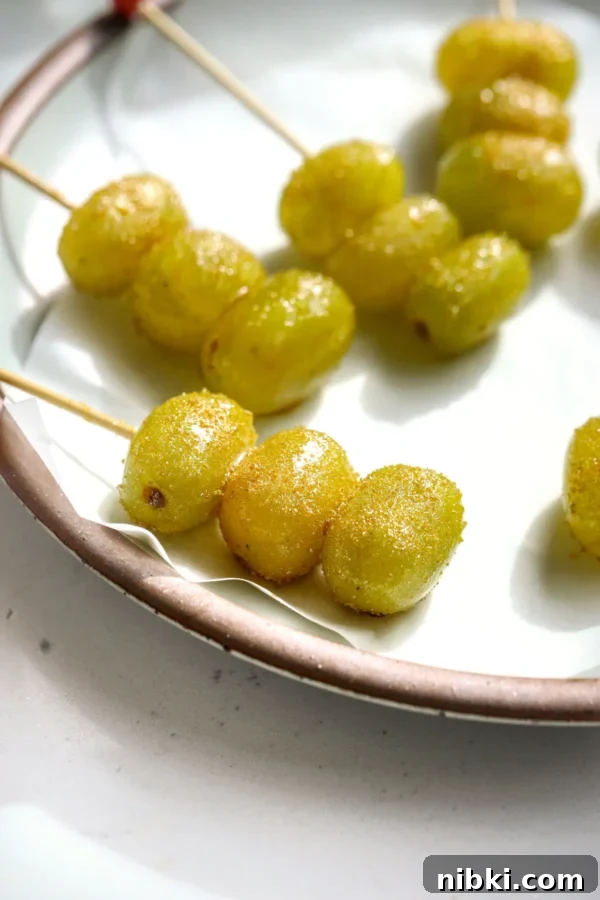 Close-up of gold-sugared champagne grapes on a wooden skewer resting on a speckled cream plate.