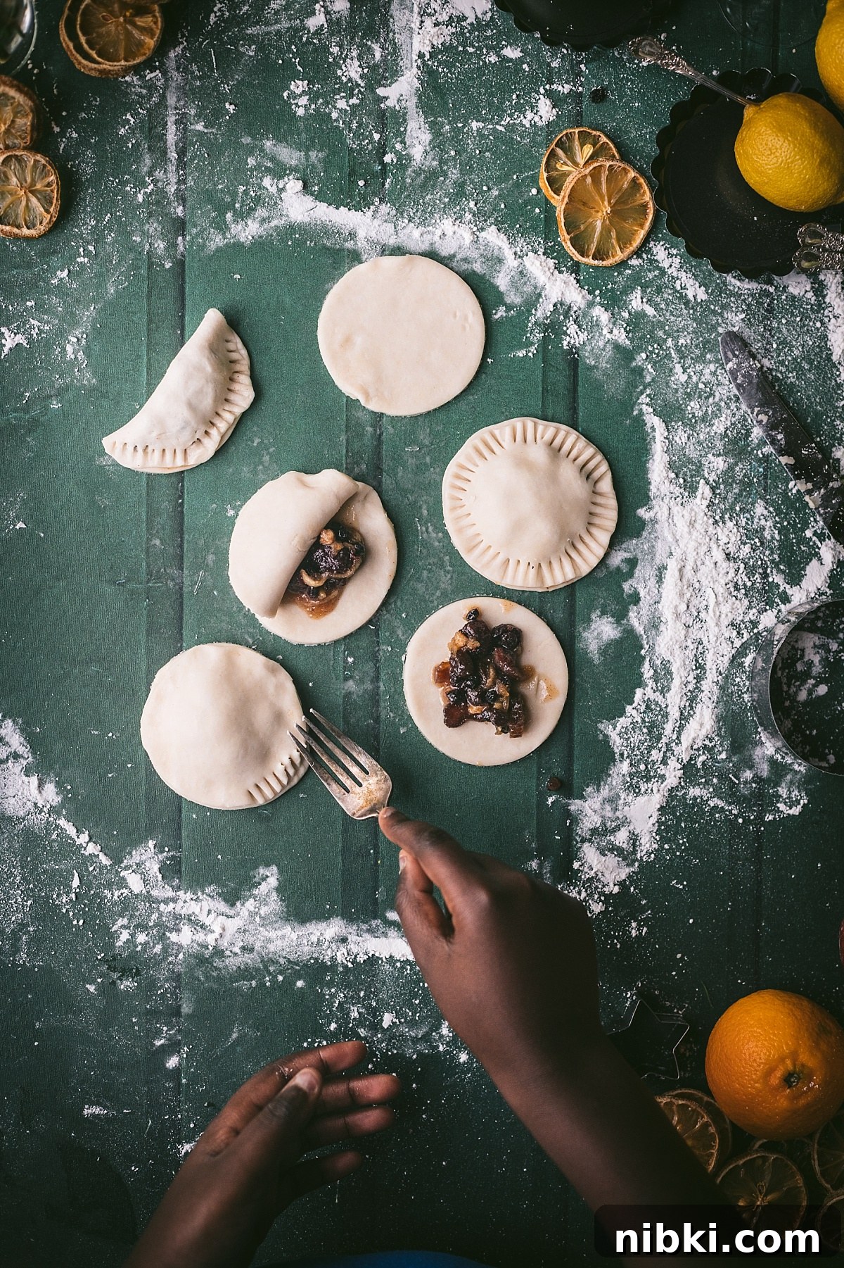 overhead shot of kids hand using fork to crimp edges of a christmas pie. other tarts show mince filling
