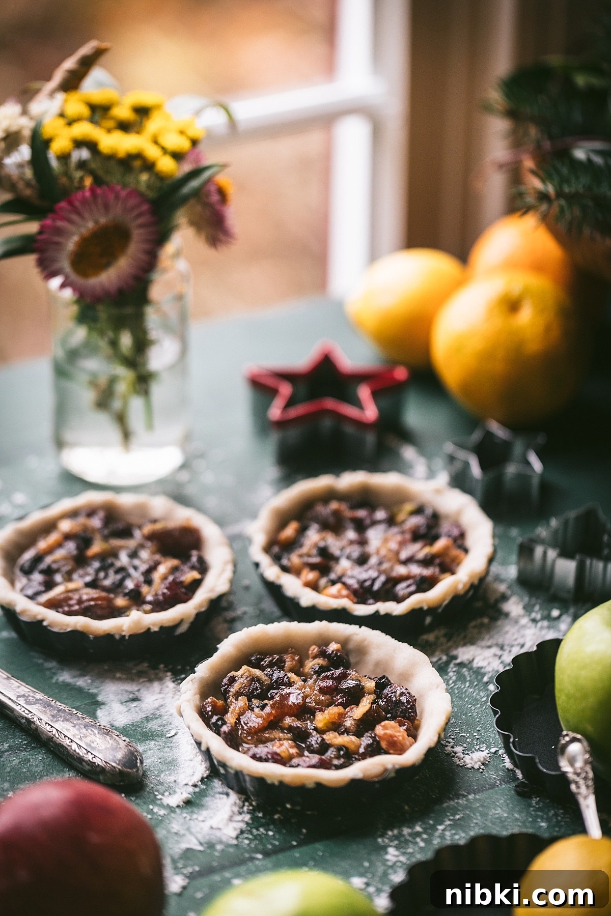 backlit shot of 3 tarts filled with mince filling but not yet topped. window lit flowers in background