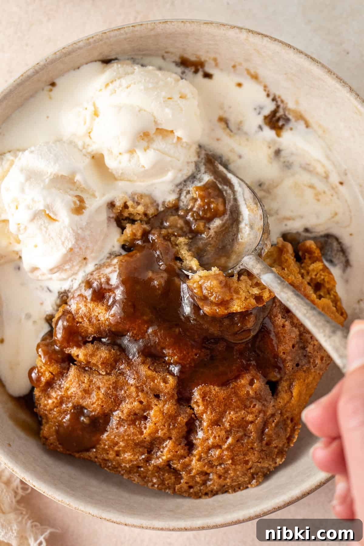 A bowl of butterscotch self saucing pudding with ice cream.