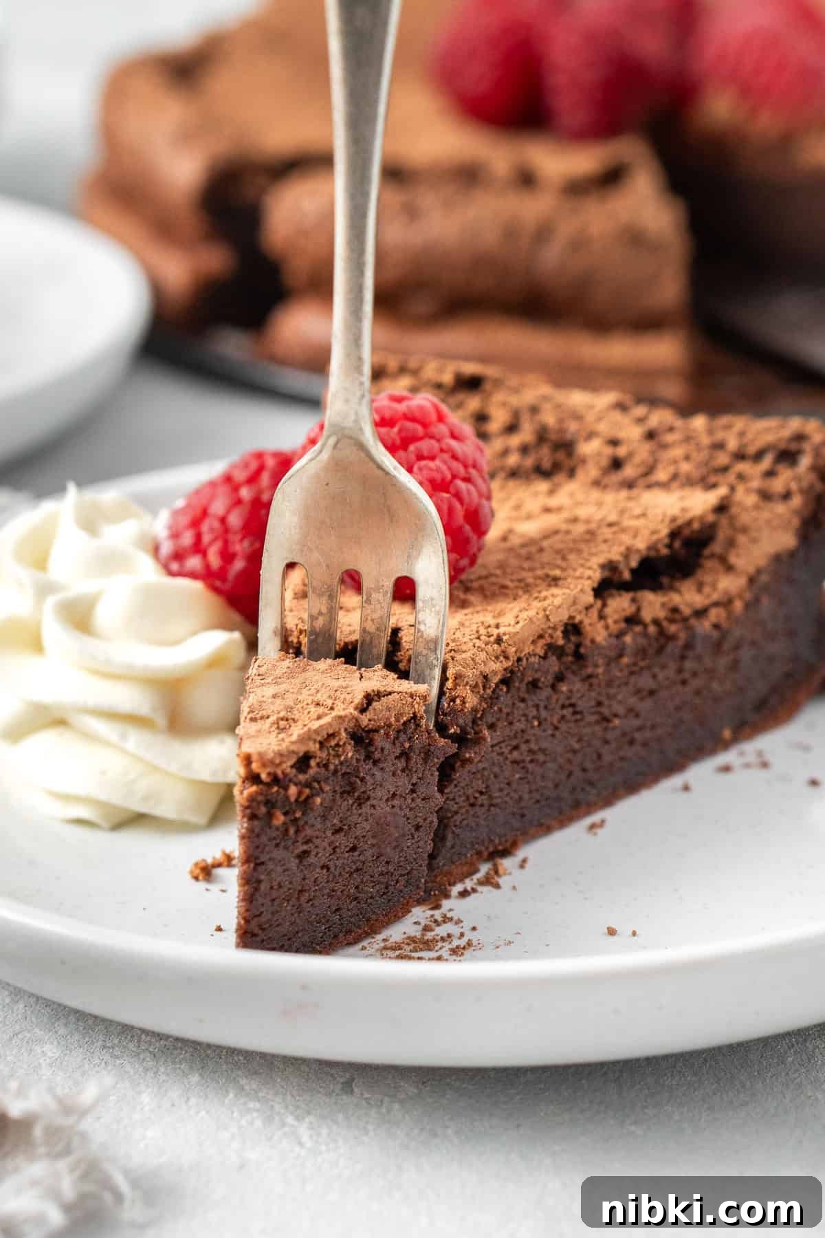 A fork taking a bite of chocolate torte on a white plate.