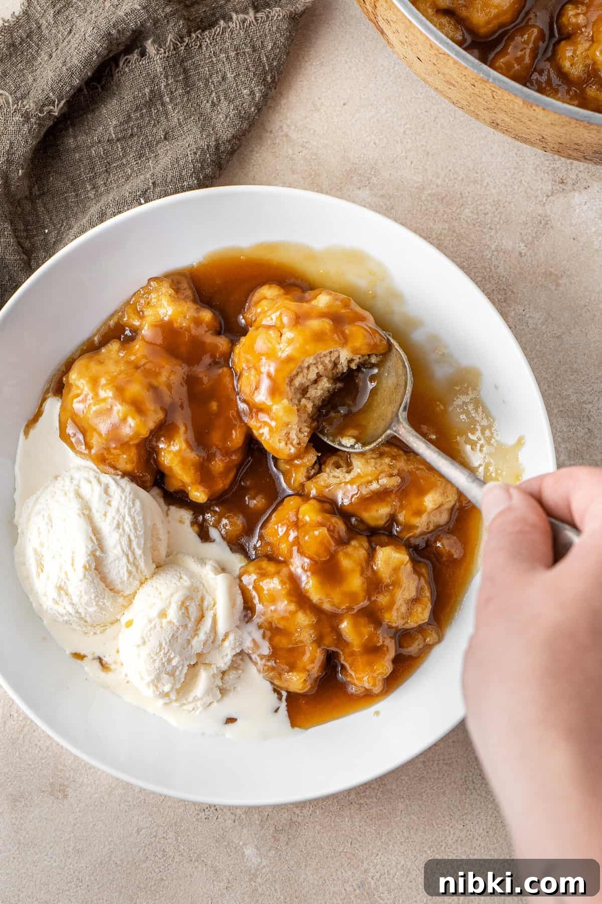 A hand taking a bite of golden syrup dumplings with ice cream.
