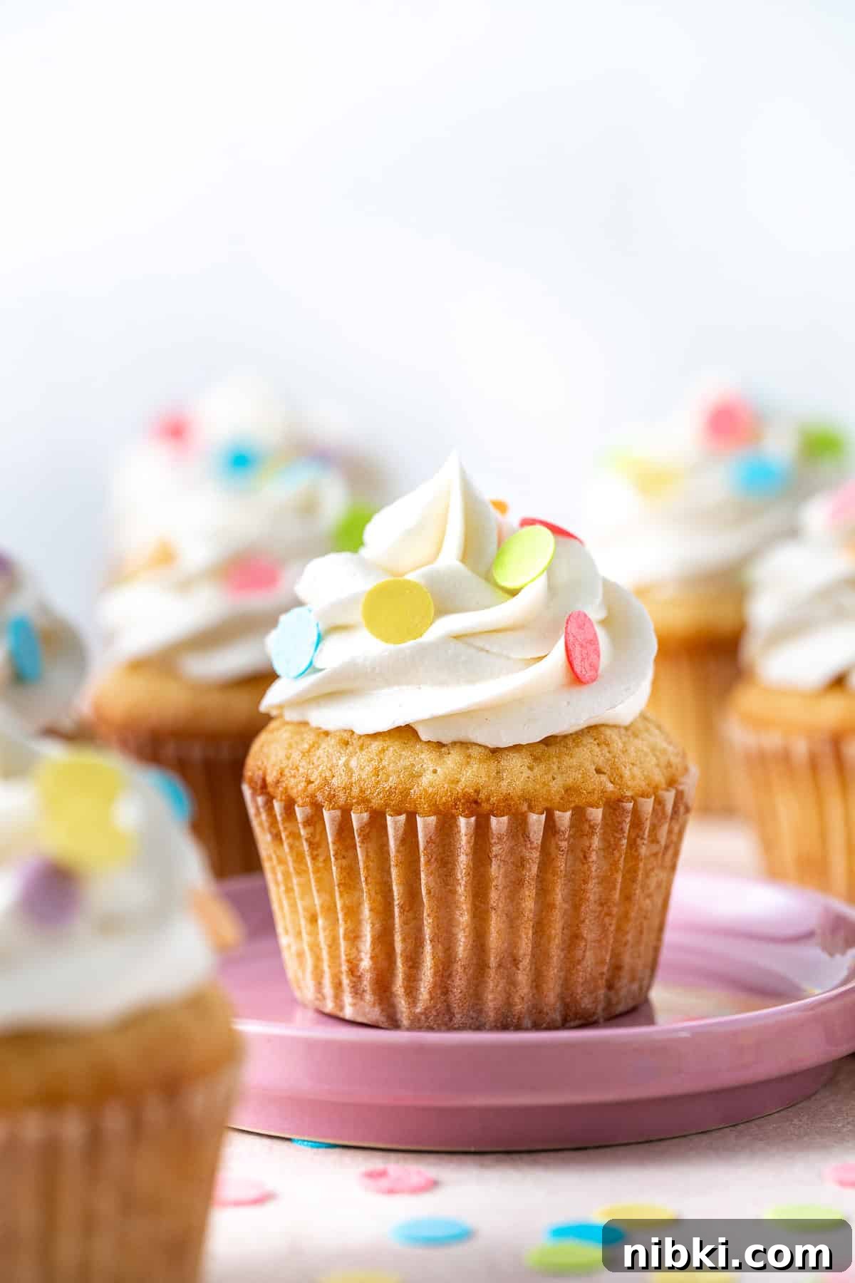 A vanilla cupcake on a pink plate with sprinkles.