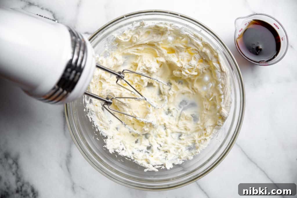 Process shot showing beaters mixing cream cheese for the maple cream cheese frosting recipe.