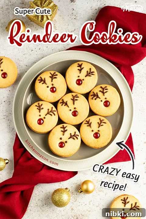 A plate of Reindeer cookies set on a second plate and a red linen napkin. Set on an off white backdrop with golden baubles, golden presents and more reindeer cookies in the background.
