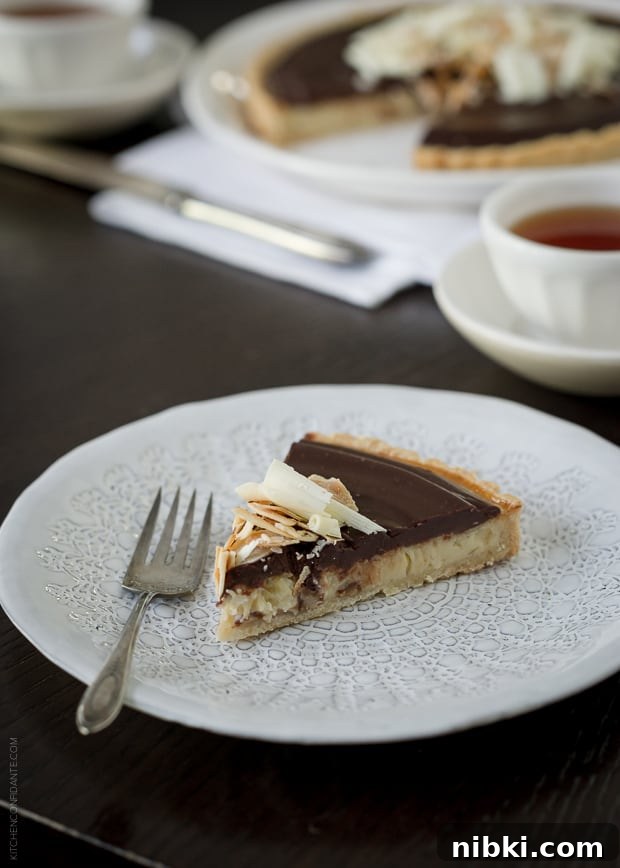Coconut Custard Tart with Chocolate Ganache Recipe 8 A slice of chocolate-topped coconut tart served on a plate with a fork.