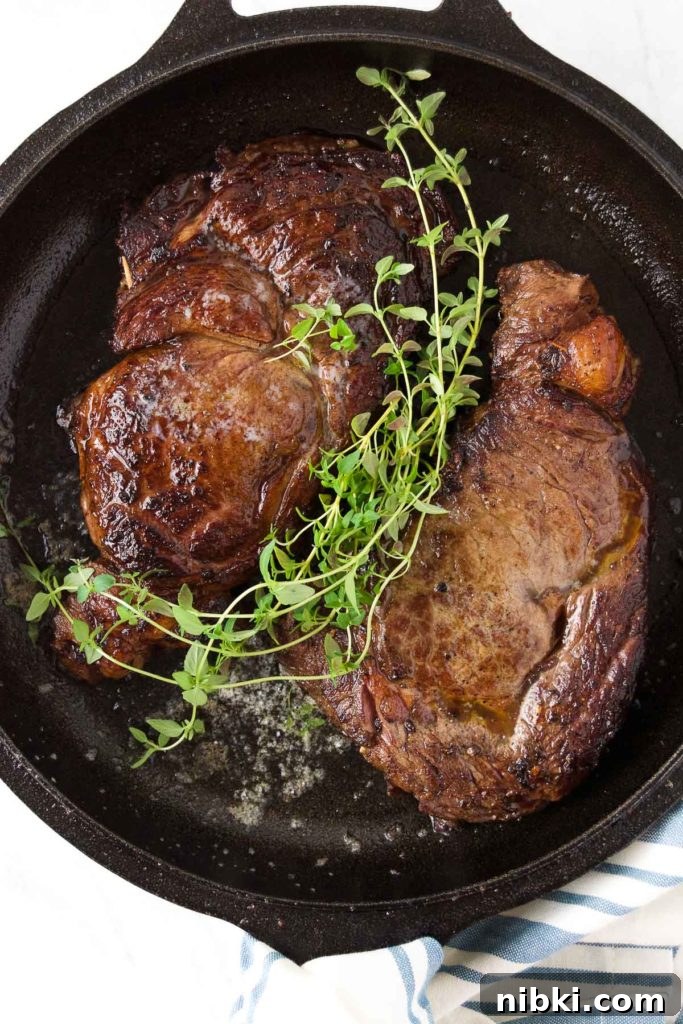 Garlic Herb Ribeye Steak Marinade for Grilling 3 Two ribeye steaks in a skillet topped with fresh thyme